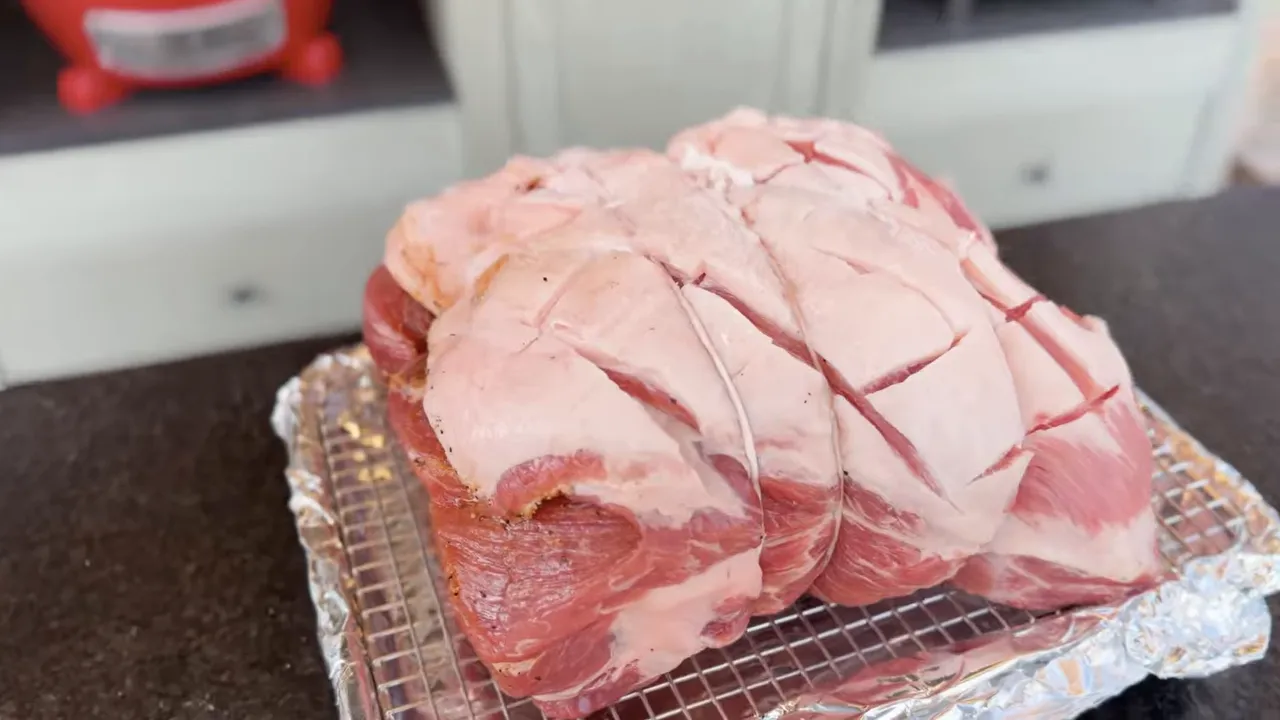 Raw pork shoulder with a crosshatched scored surface in a foil tray