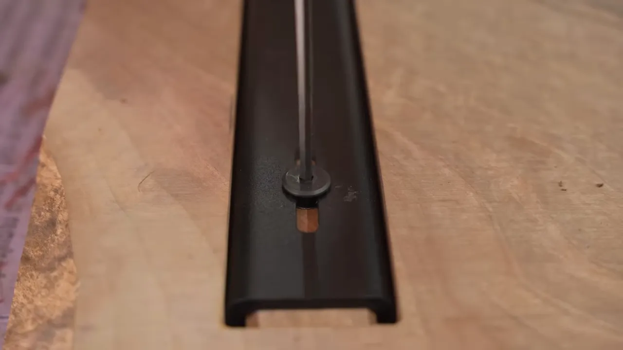 A black steel C-channel recessed into a walnut tabletop with bolts along its length
