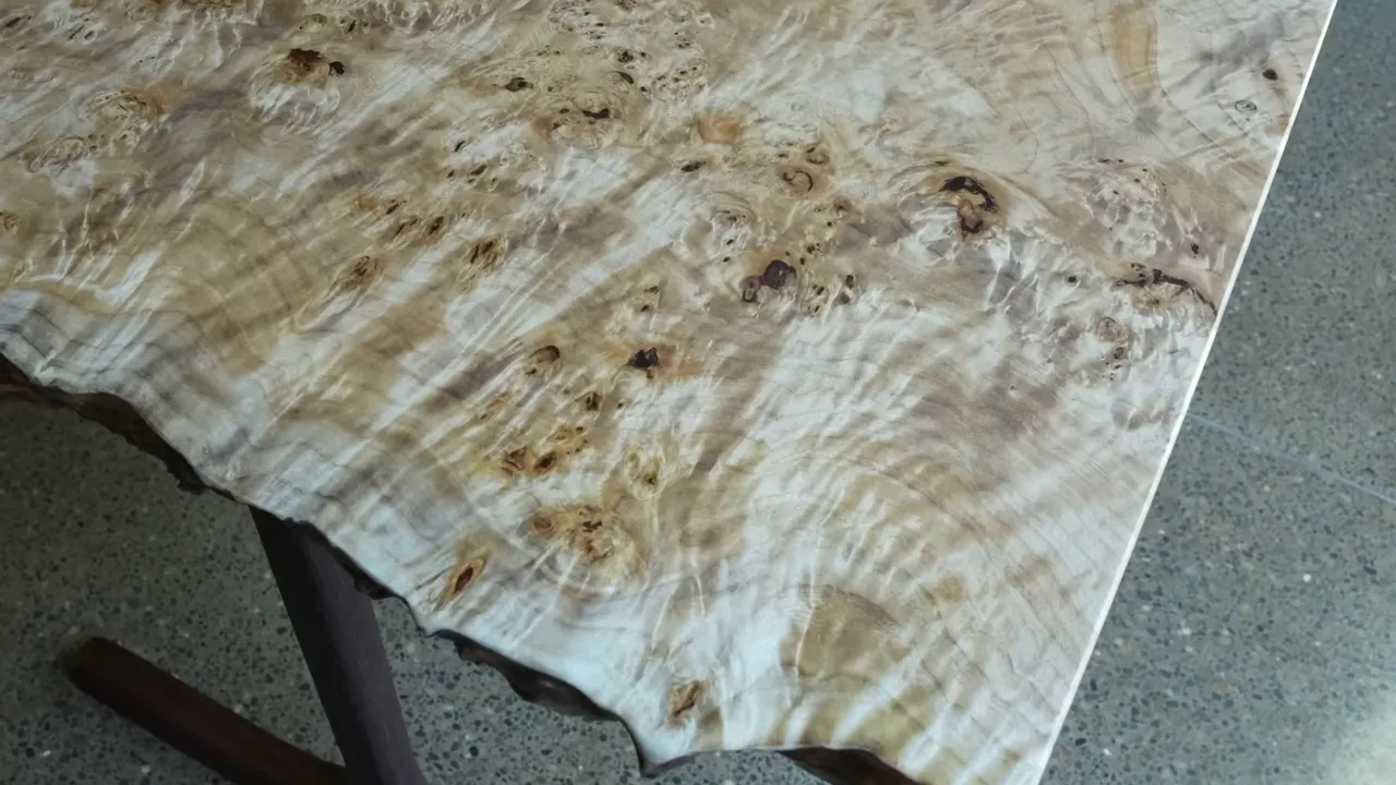 Finished pale burl tabletop with a reflective surface, irregular end, and straight beveled side