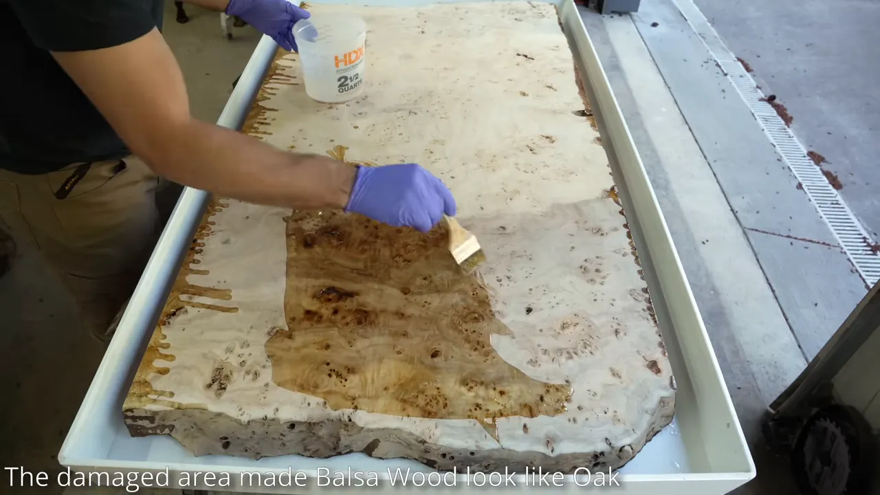 A gloved hand brushing epoxy across a burl slab inside a white tray