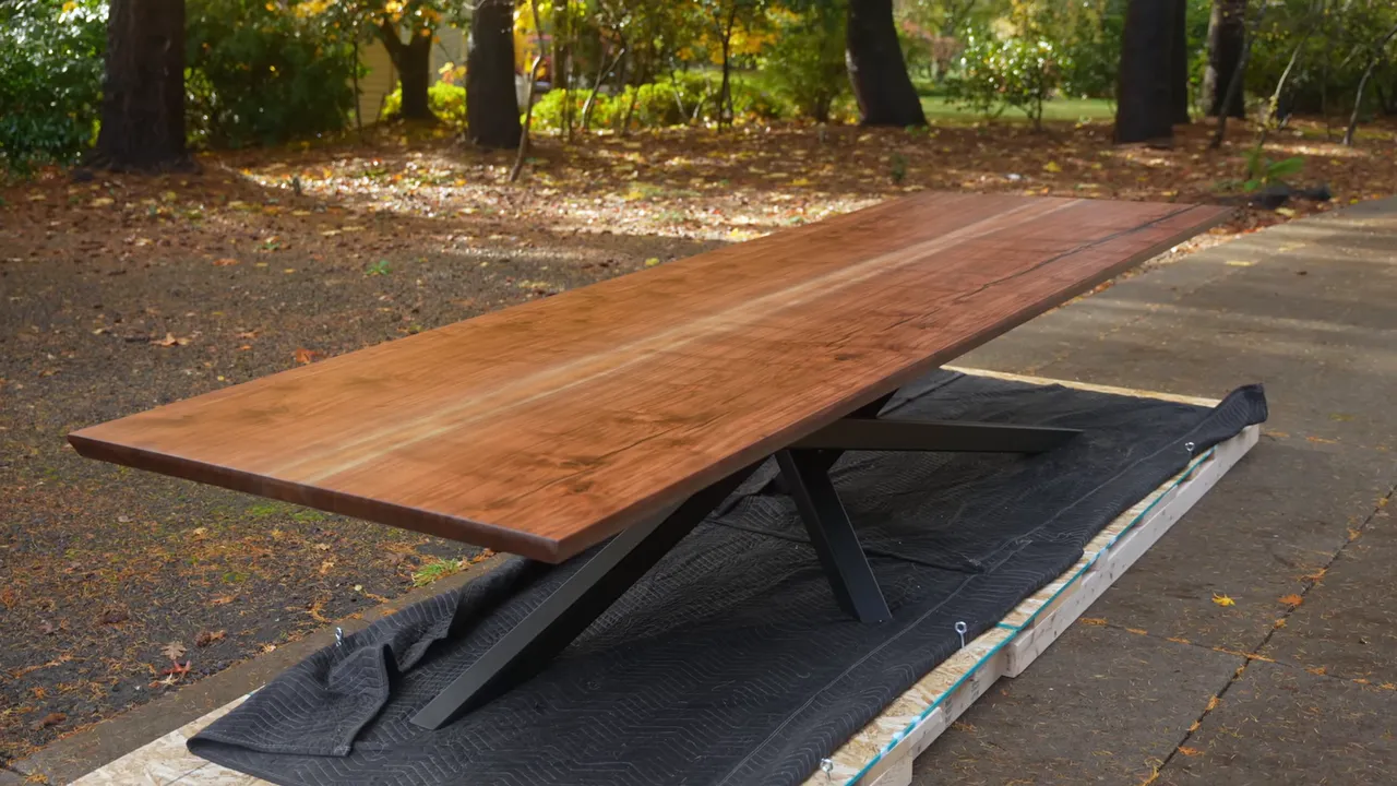 Finished long walnut table with black steel base sitting outdoors on a wooden shipping platform