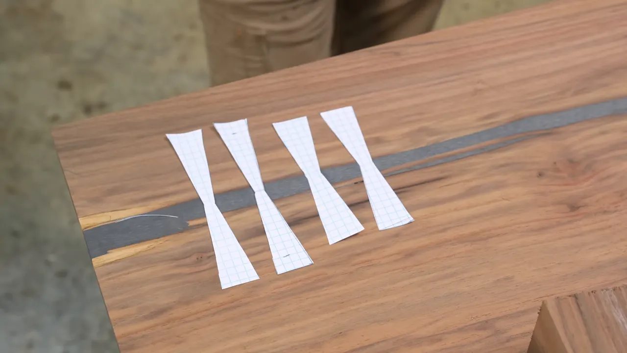 White paper bow tie templates in two sizes arranged across an epoxy-filled crack in walnut
