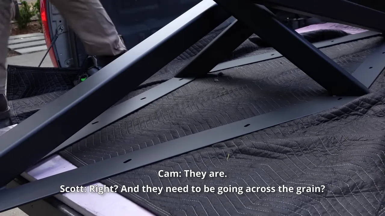 Close view of elongated mounting holes in a black steel table base resting in a pickup bed