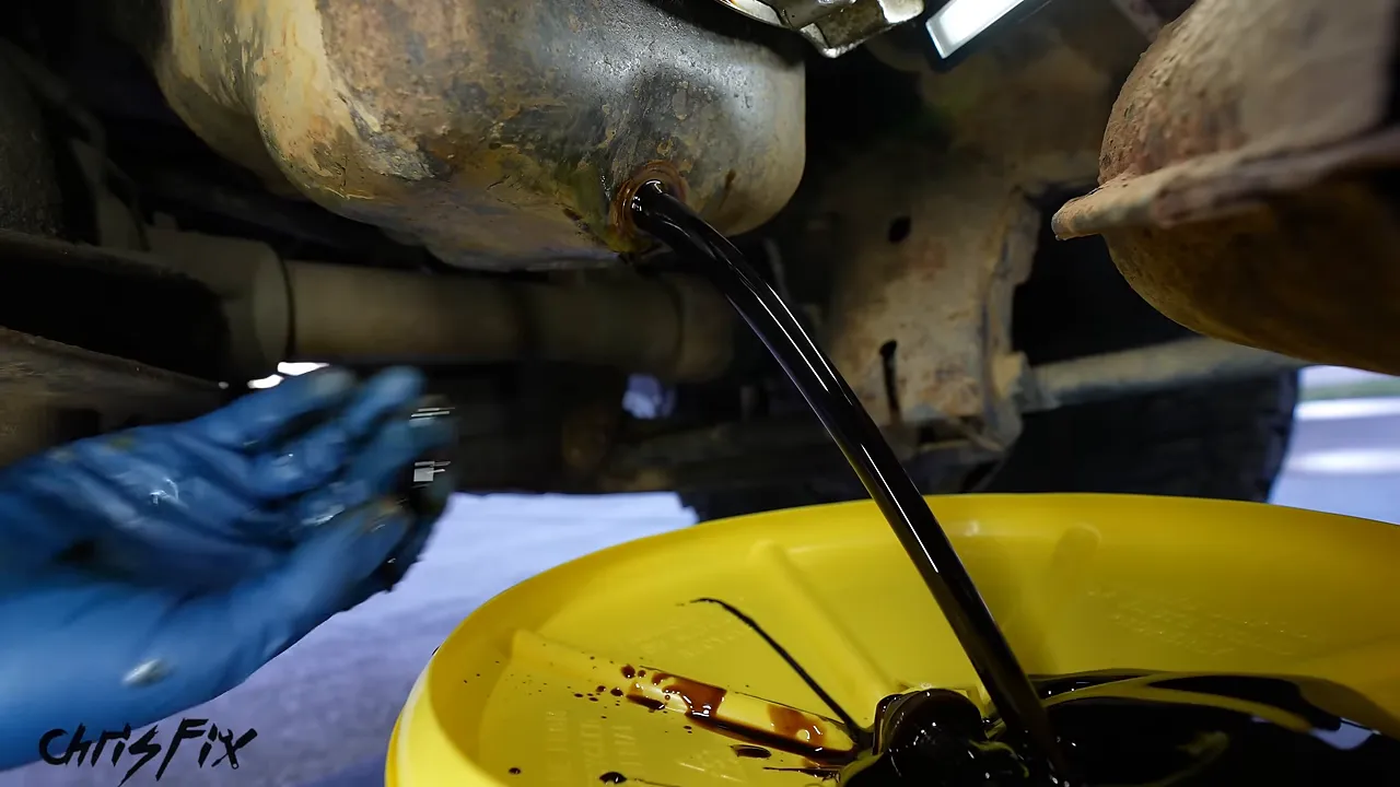 Oil draining from a vehicle into a raised yellow funnel beneath the drain opening