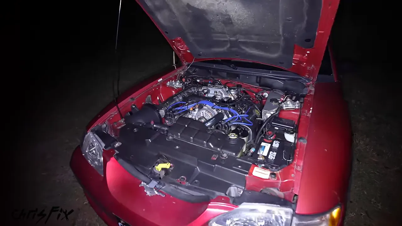 Red car engine bay illuminated at night beneath an open hood
