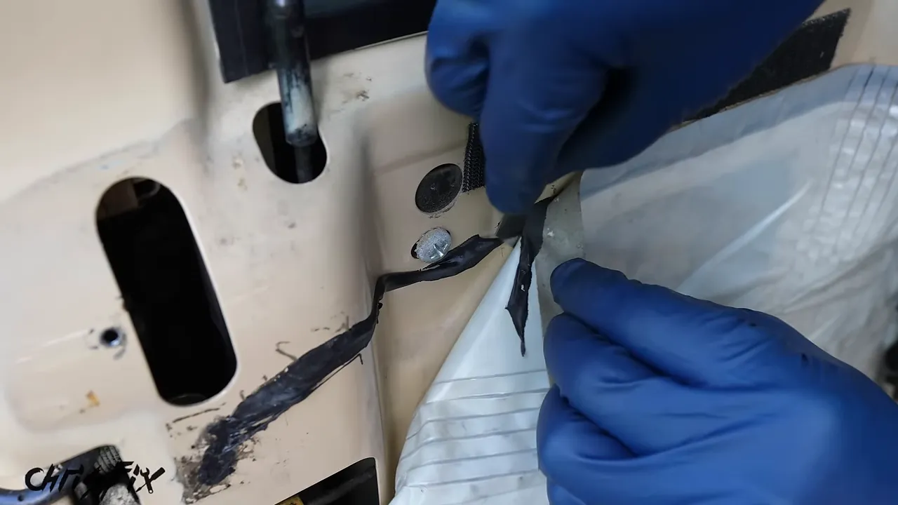 Gloved hands separating the plastic door moisture barrier from black adhesive with a razor blade
