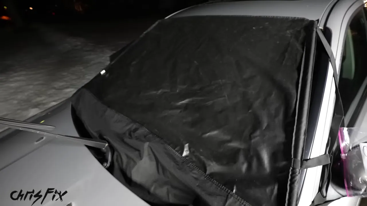 A black cover across a silver car windshield with raised wipers and a bag over the side mirror