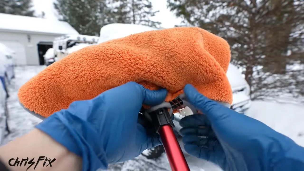 An orange microfiber towel secured around a snow brush head with black binder clips at the back