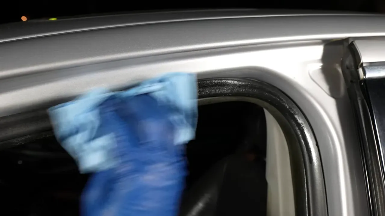 A gloved hand wiping the rubber seal around a car door opening with a blue towel