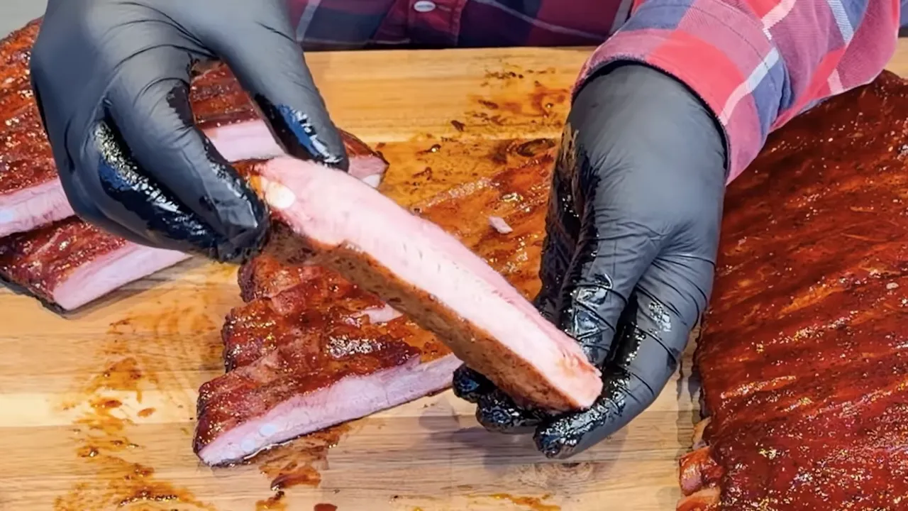 Gloved hands holding a sliced rib above a cutting board with more ribs