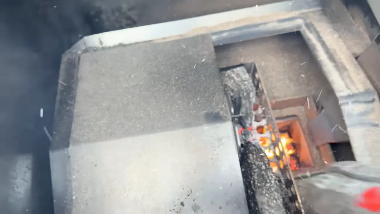 A charred wood split burning above orange flames inside the grill's metal fire opening