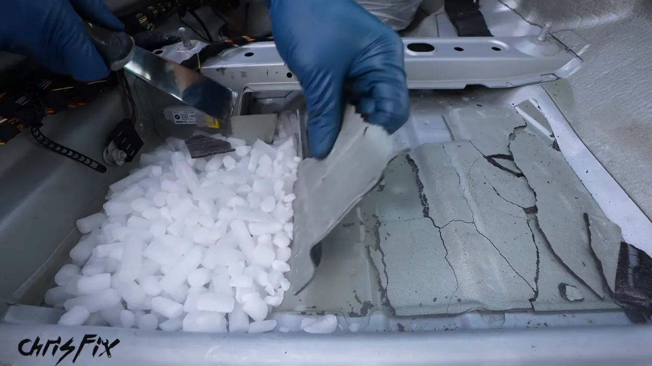 Blue-gloved hands lifting a sheet of sound deadening beside dry ice on the stripped floor
