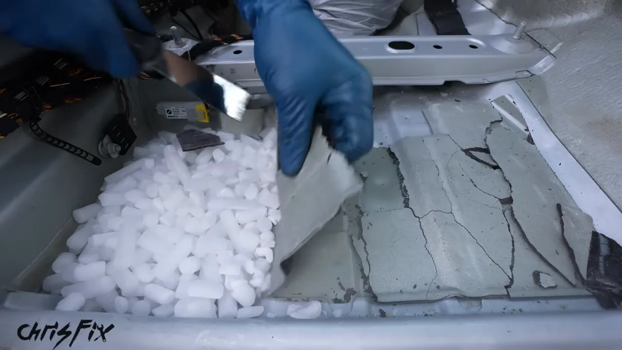 Gloved hand lifting a broken sheet of sound deadening beside dry ice pellets on the floor pan