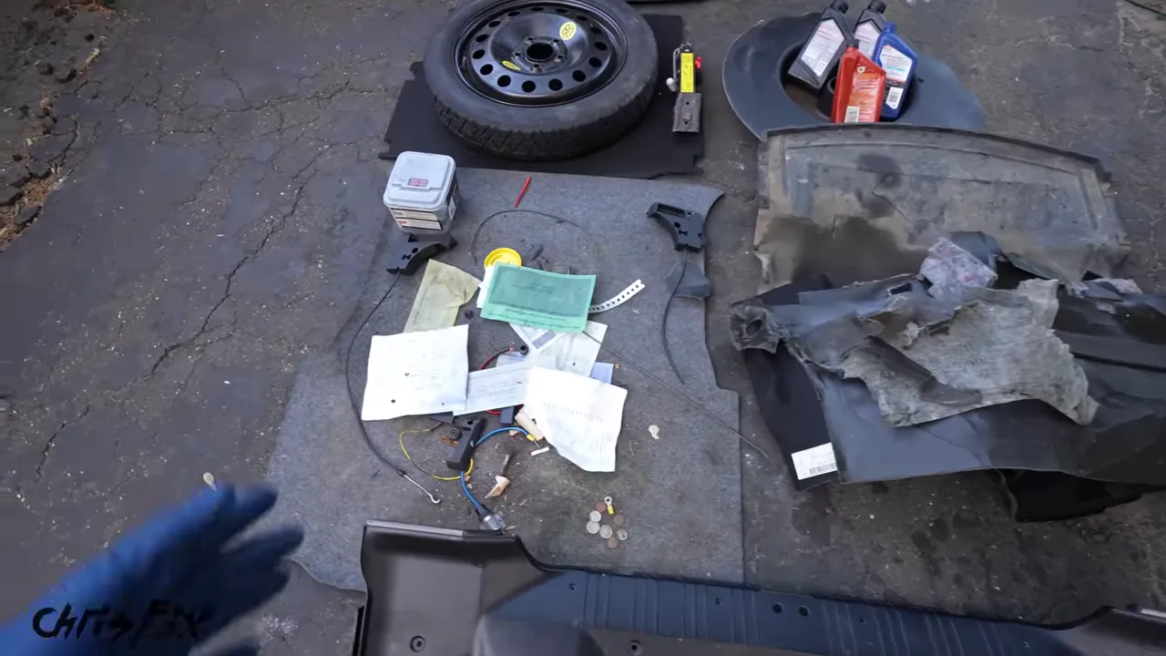 Spare tire, jack, trunk liners, plastic panels, and supplies laid out on the driveway
