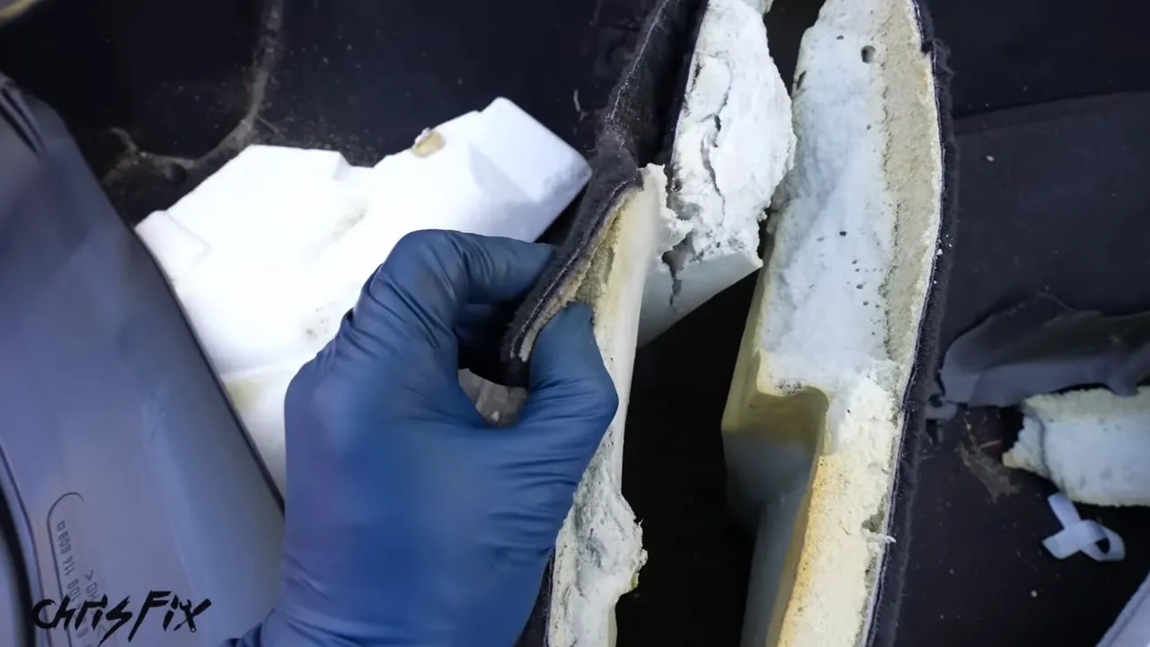 Lifted edge of black automotive carpet showing thick white insulation underneath