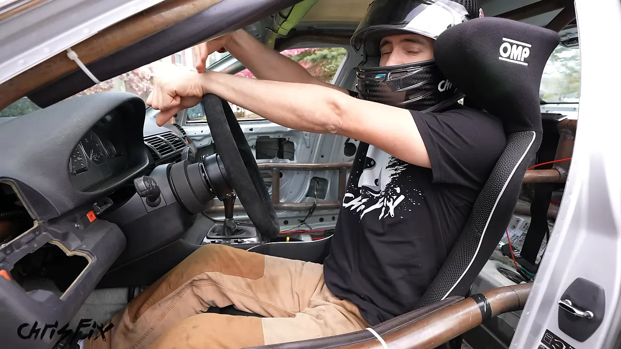 Driver seated in a racing seat with arms extended over the steering wheel