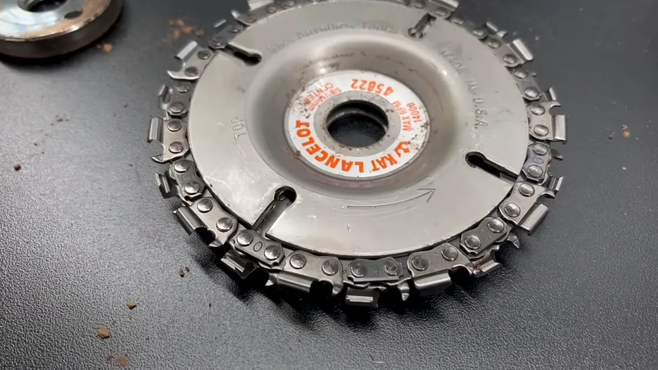 Round metal angle grinder attachment with chainsaw teeth around its outer edge on a dark work surface