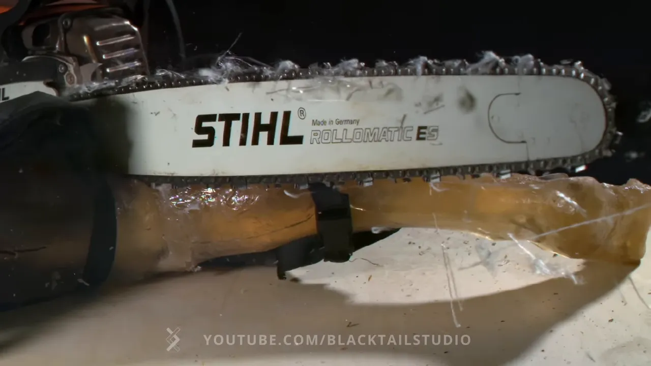 Chainsaw bar above an artificial leg with loose white fibers pulled from dark protective chaps