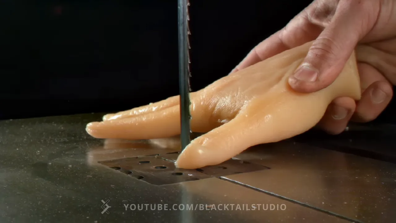 Artificial hand beside a bandsaw blade with a deep cut through the base of its thumb
