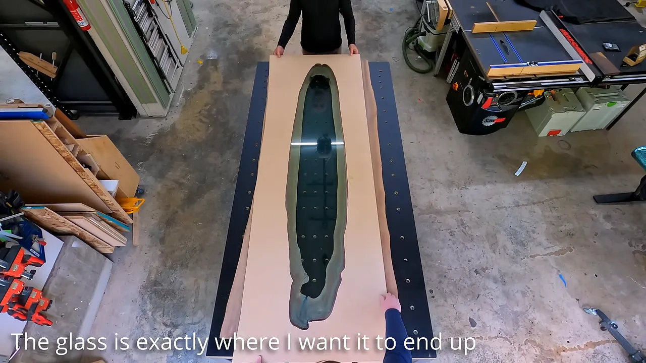 Overhead view of a long glass panel positioned inside a routing template on the walnut slab