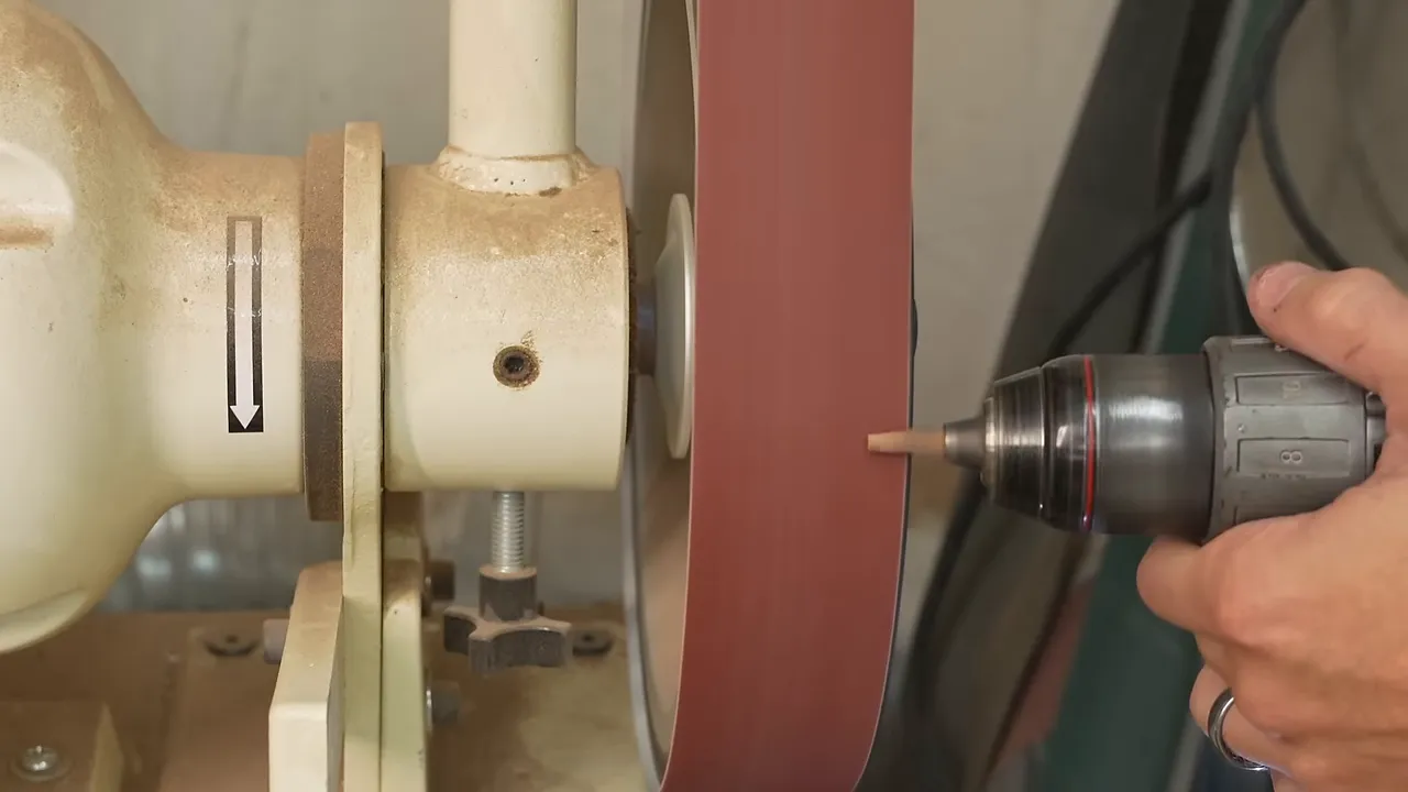 A drill holding a small wooden plug against a vertical sanding disc
