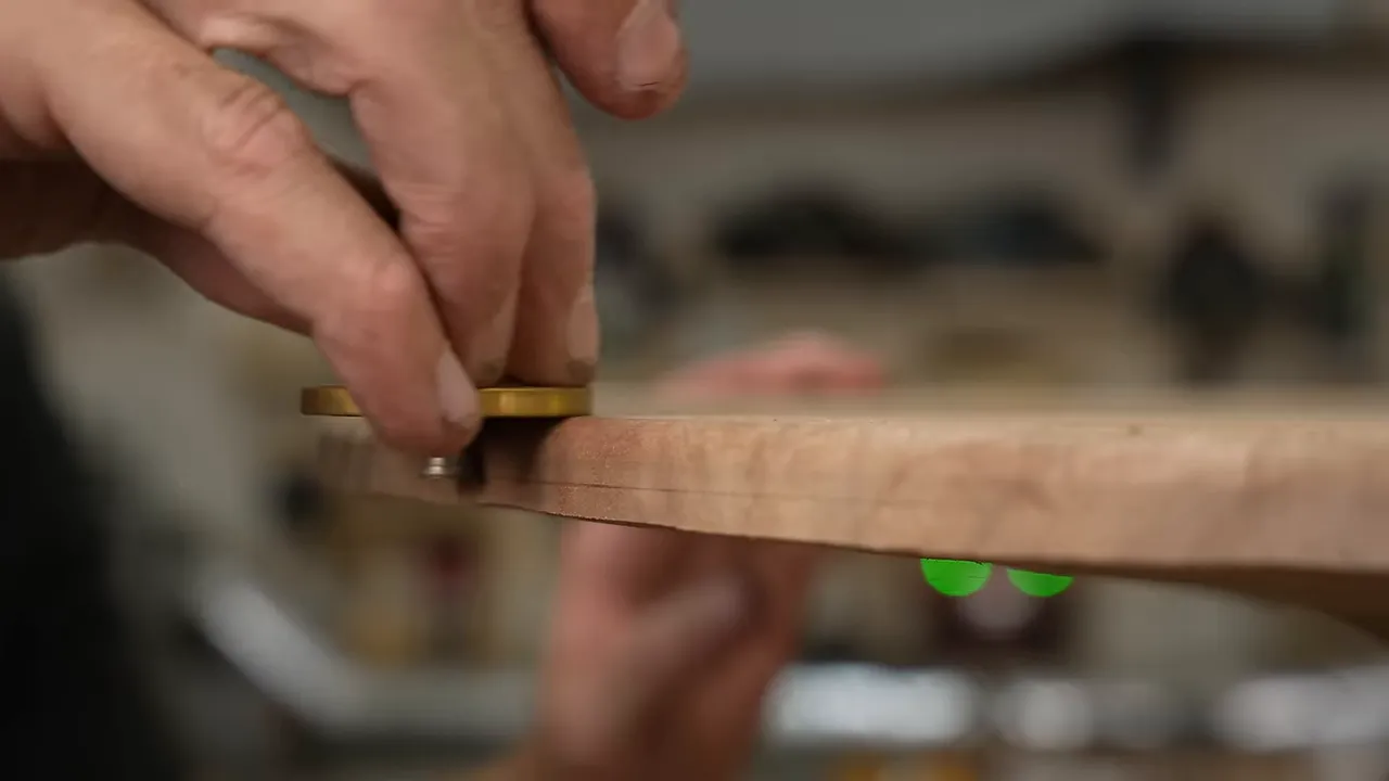 A brass marking gauge scribing a line along the edge of a wooden tabletop
