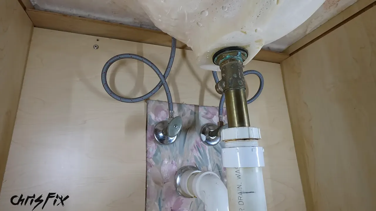 New braided supply hoses routed in loops beside the old metal drain and white P-trap