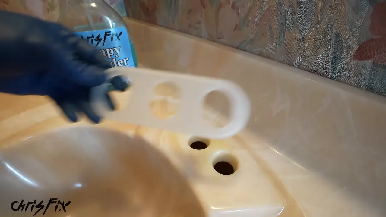 Gloved hand holding a three-hole faucet gasket above the cleaned sink mounting holes