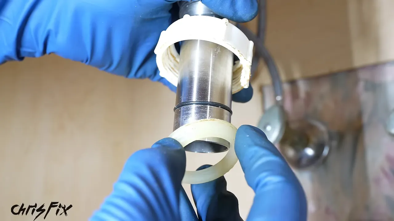 Gloved hands positioning a tapered slip-joint washer below a white nut on the metal drain tailpiece