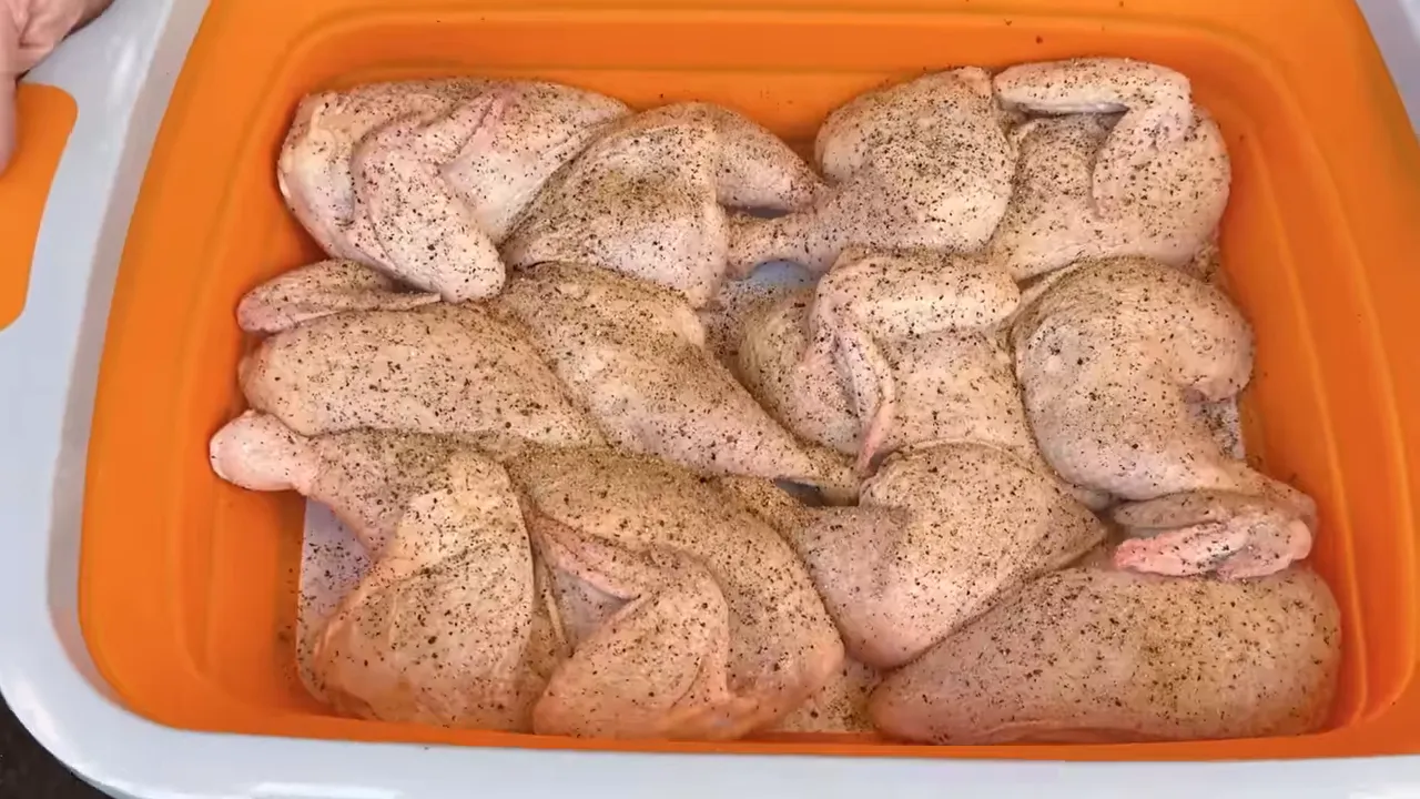 Six seasoned raw chicken halves arranged skin side up in a large tray