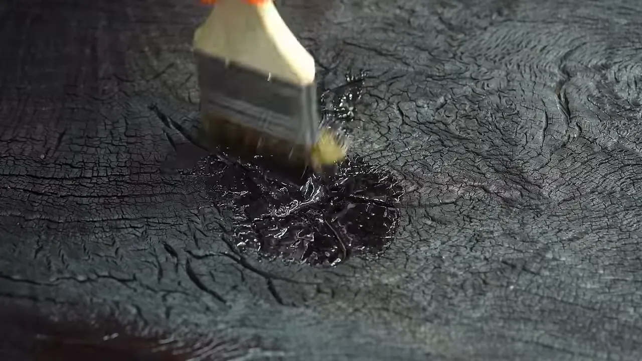 Brush applying epoxy to the cracked black surface of the charred oak