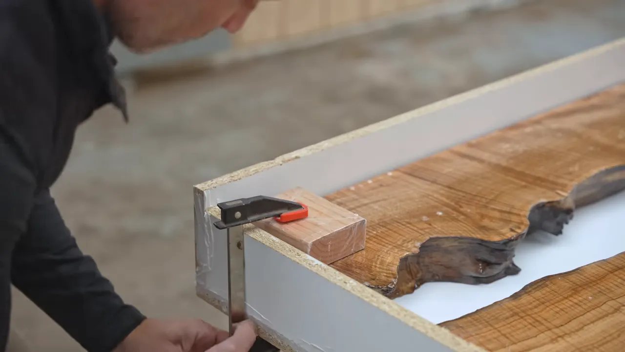 Clamp holding a crosspiece over maple slab sections inside a white mold