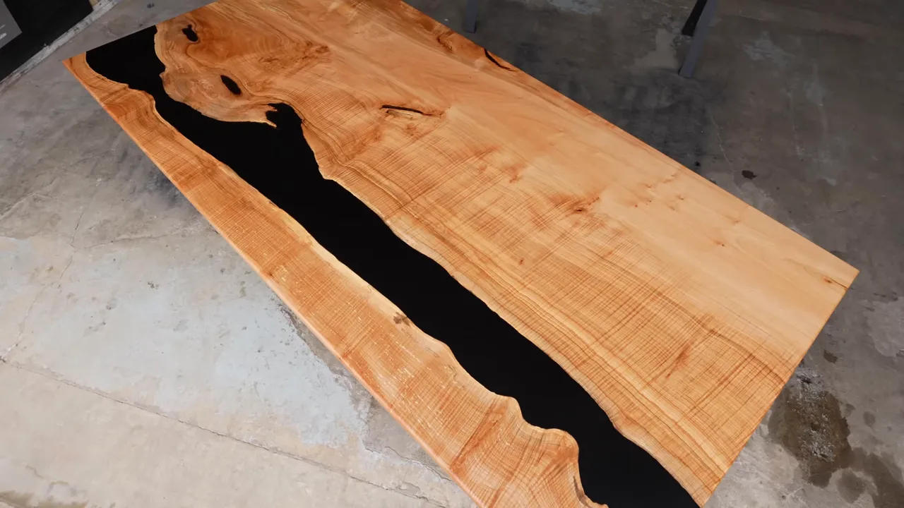 Finished light maple dining tabletop with black resin following irregular natural wood edges