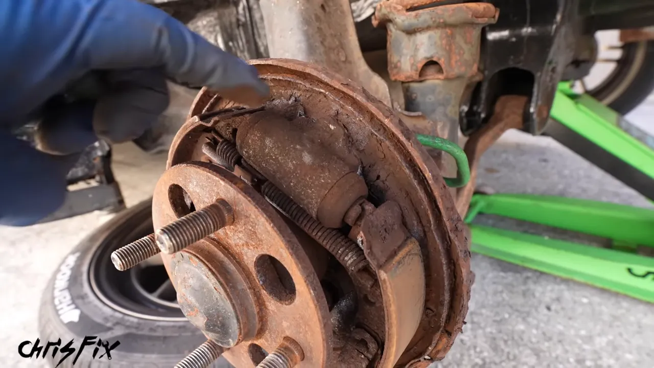Rear drum brake with the drum removed, exposing rusty shoes and hardware