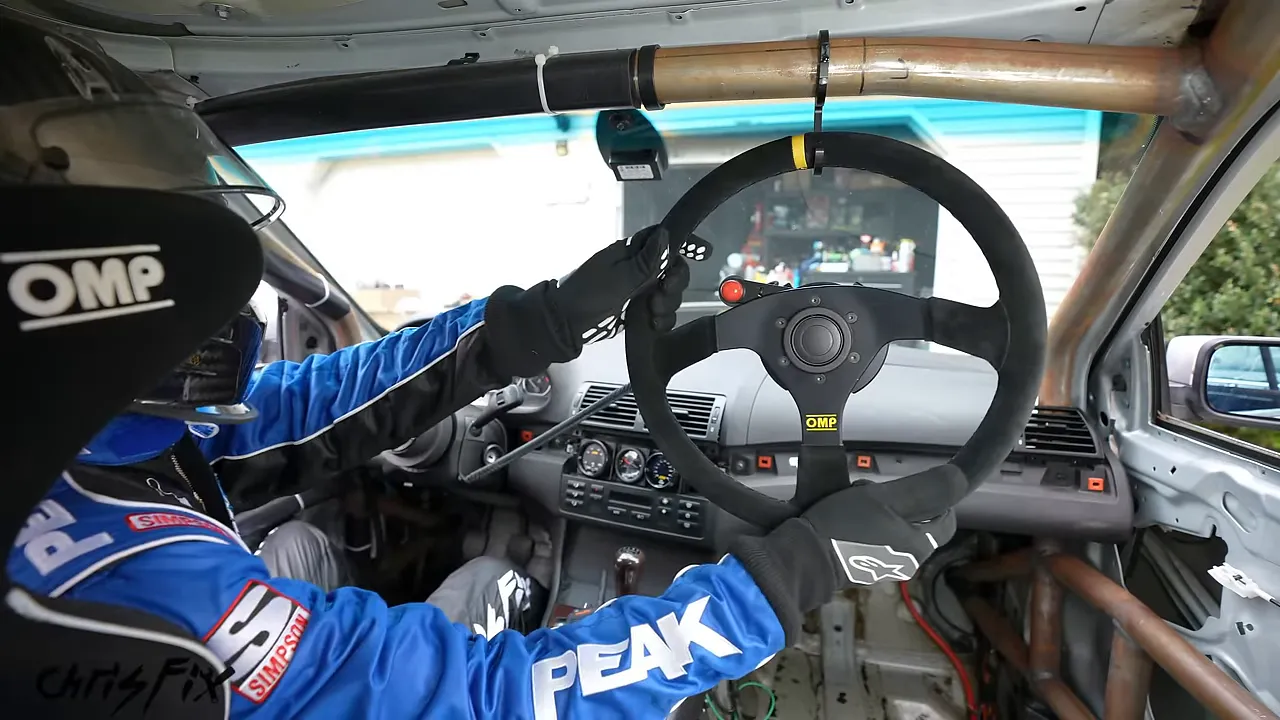 Driver holding the removed steering wheel beside the exposed quick-release hub inside the roll cage