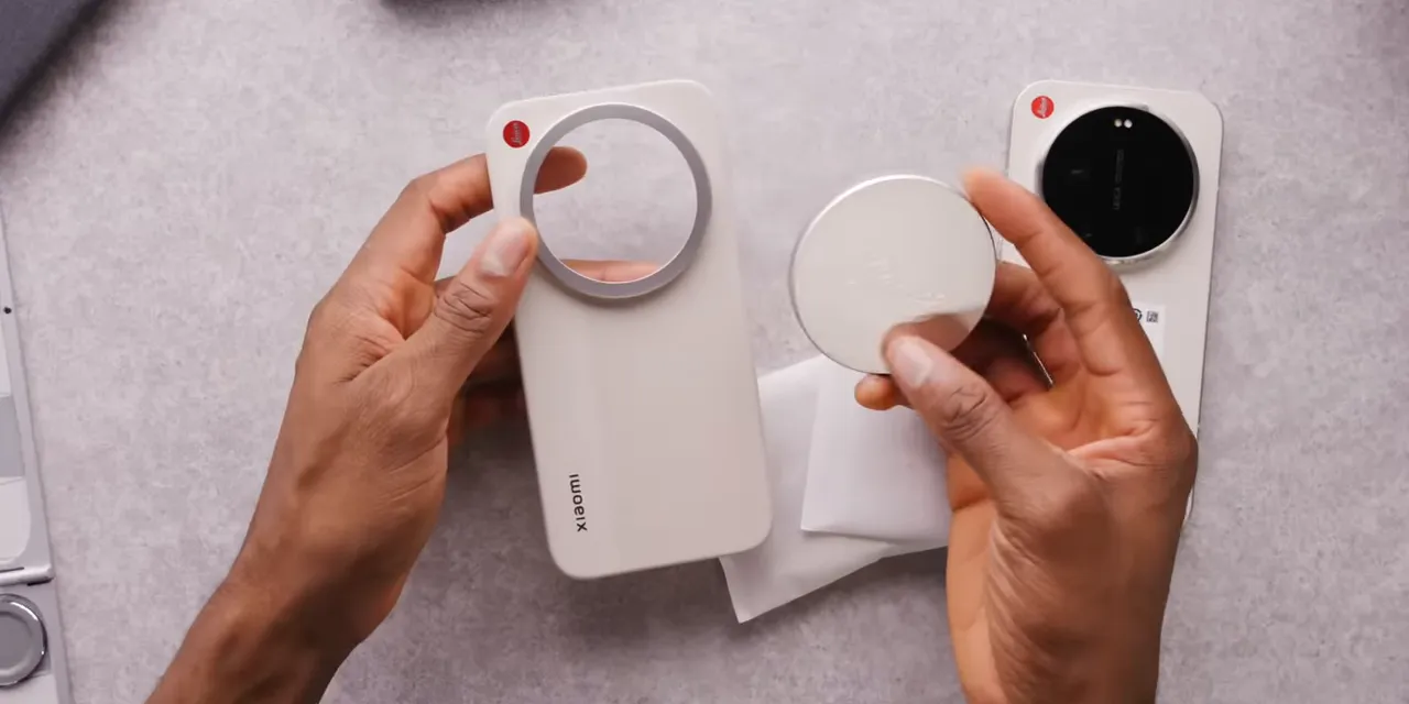 Hands holding a silver Leica lens cap against the cream phone case beside the phone