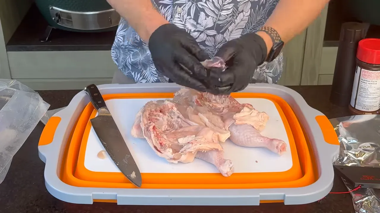 Gloved hands holding a removed chicken keel bone above an opened raw chicken