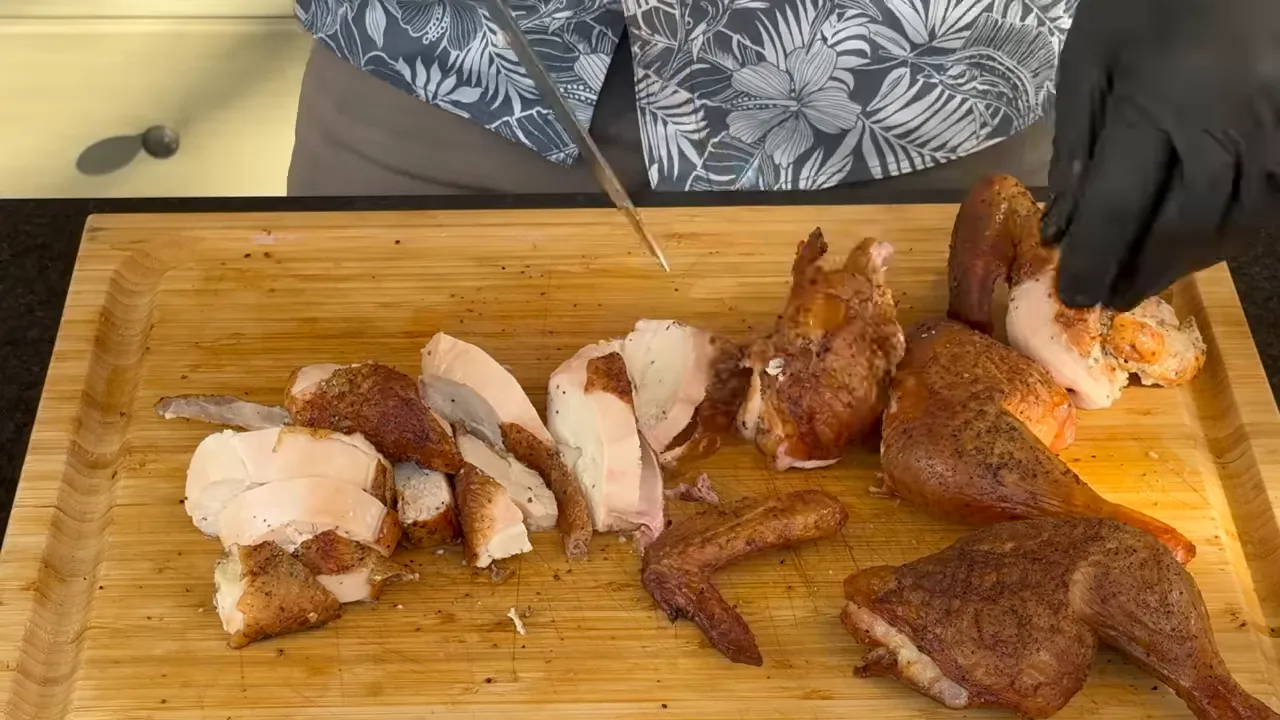 Sliced smoked chicken breast and browned leg portions on a wooden cutting board