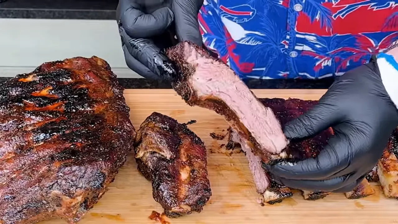 Gloved hands holding a sliced beef rib above a board with cooked ribs