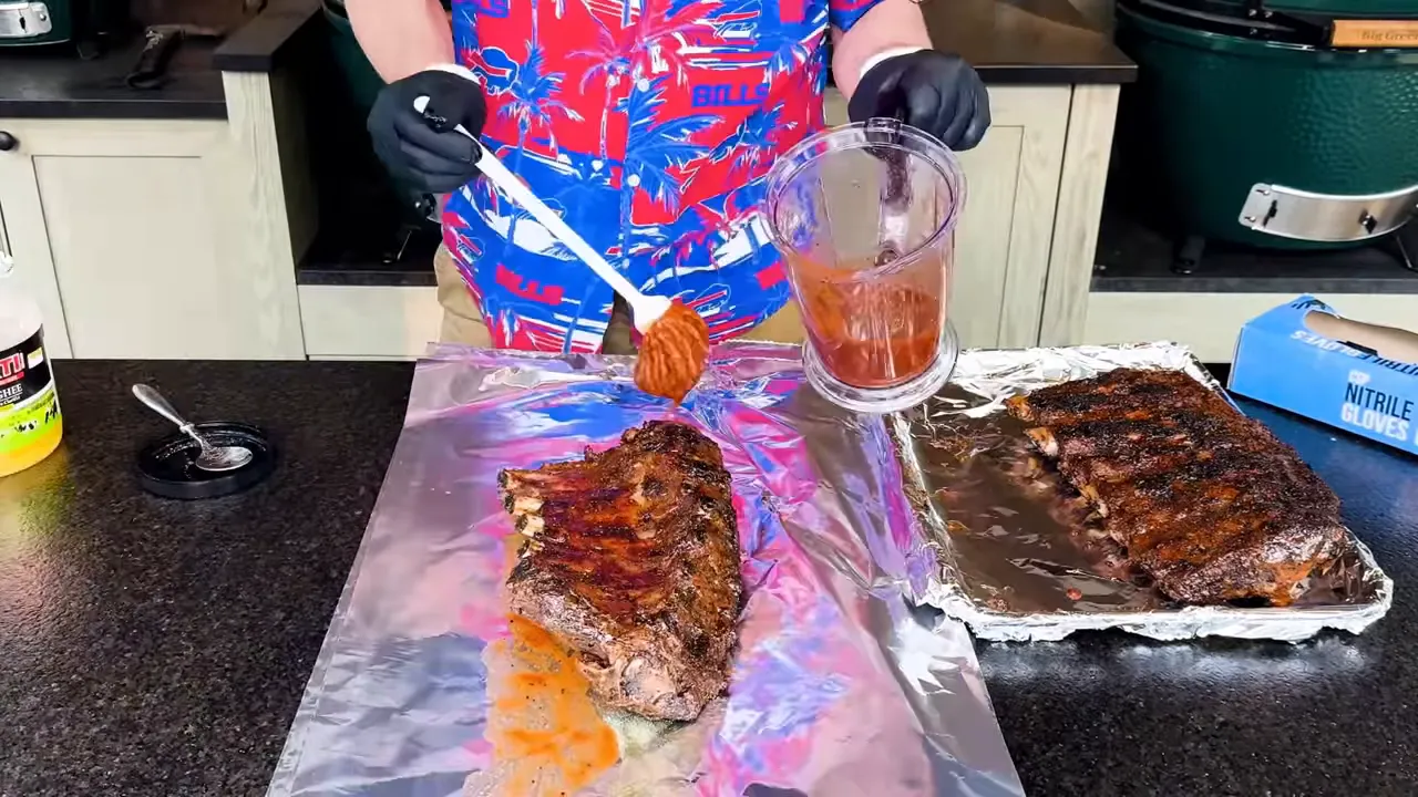Gloved hands folding foil around a glazed rack of beef ribs on a counter
