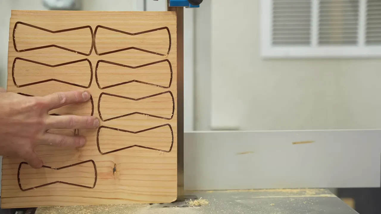 A board with multiple bow tie outlines beside a bandsaw blade