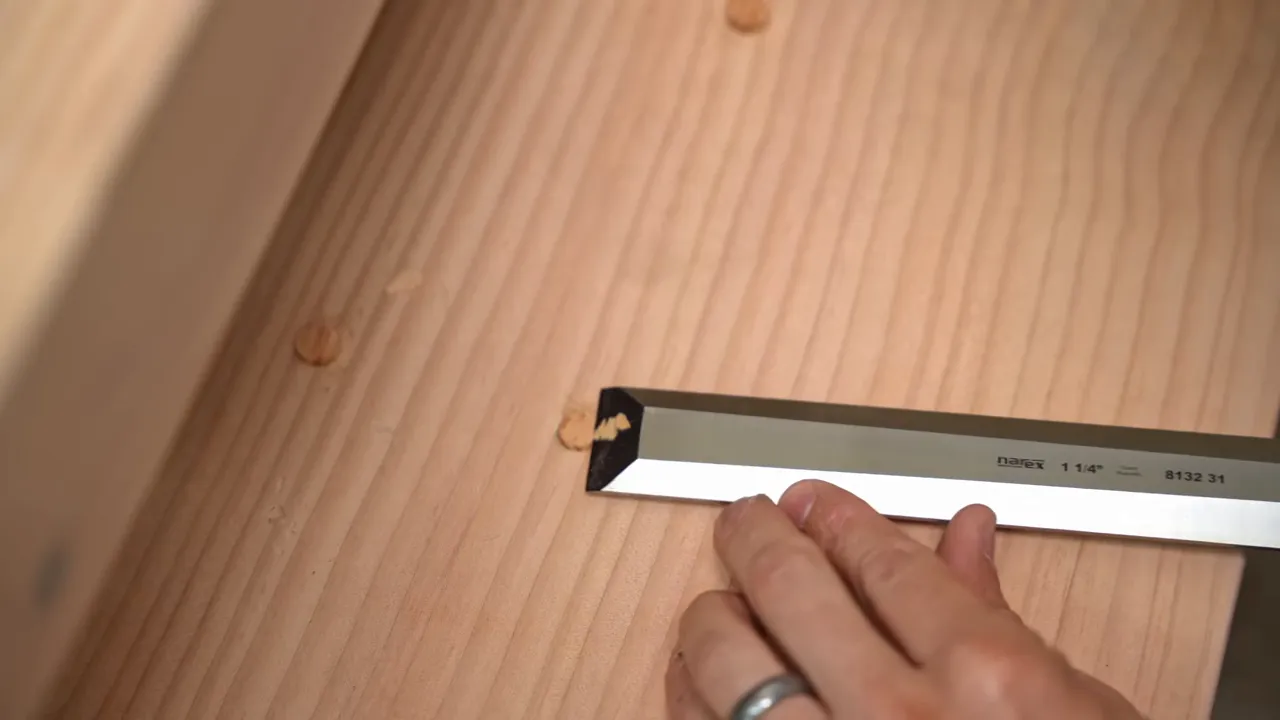 A chisel paring a round wood plug flush with a fir stair tread