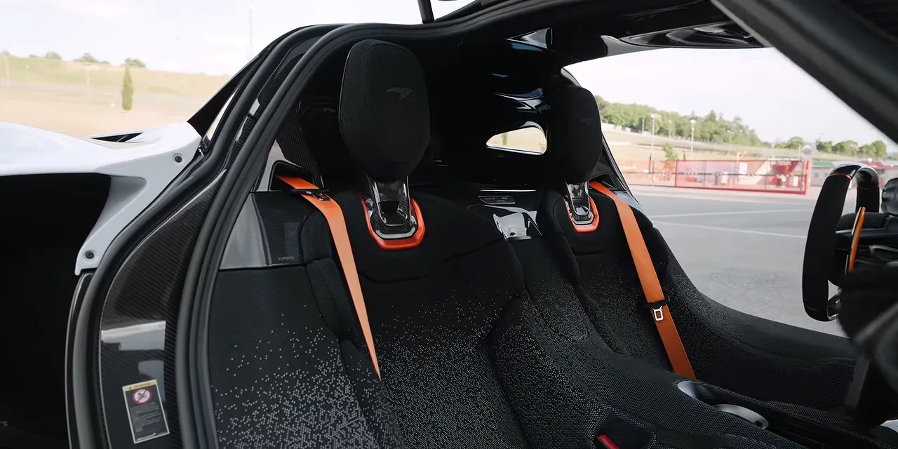 McLaren W1 fixed seats with patterned upholstery, orange seat belts, and exposed carbon fiber