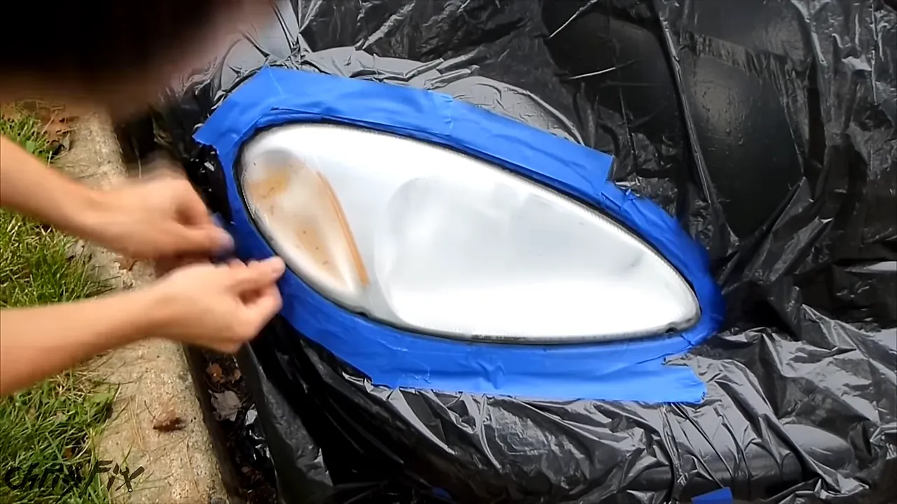 Headlight exposed through black plastic masking with blue tape sealing the opening