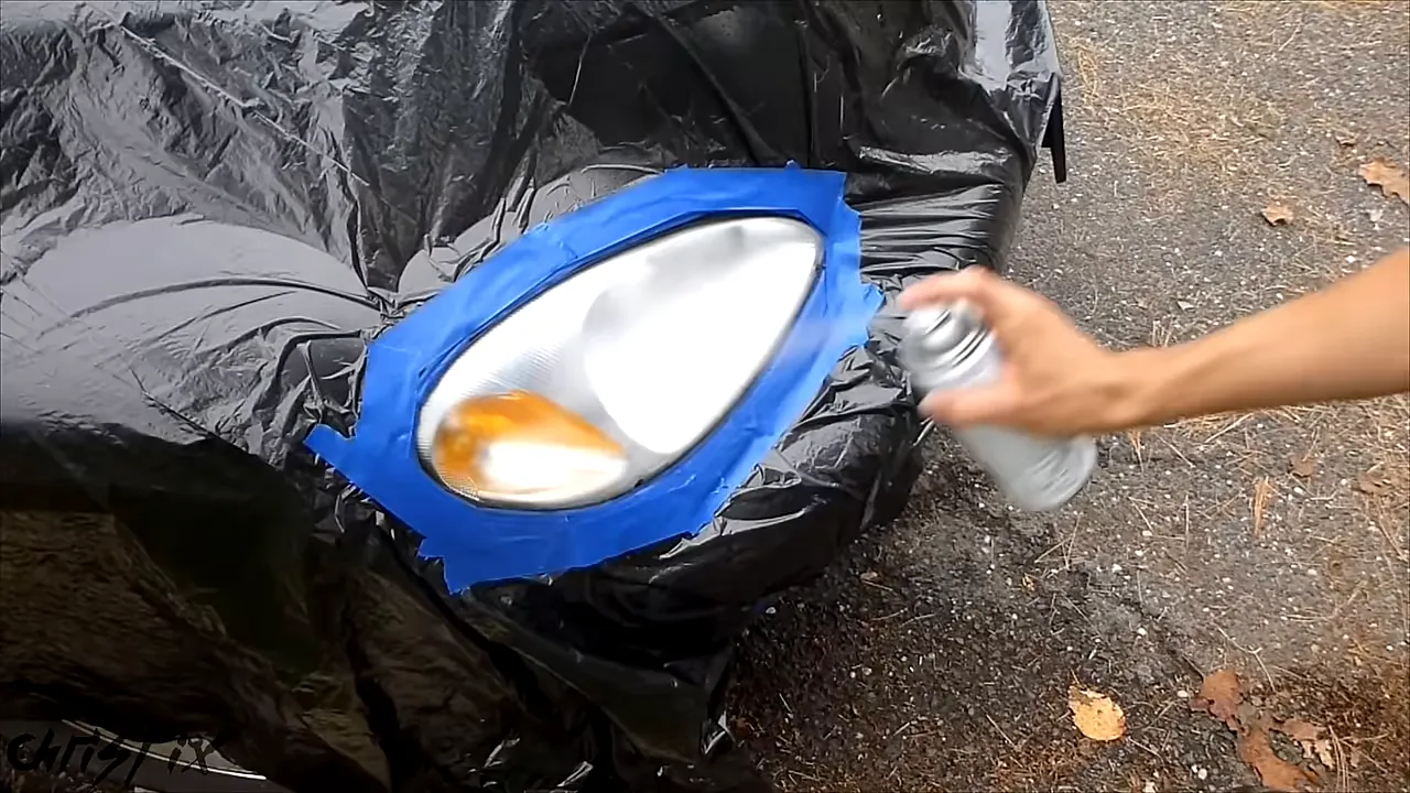 Aerosol clear coat being sprayed across a headlight surrounded by tape and black plastic