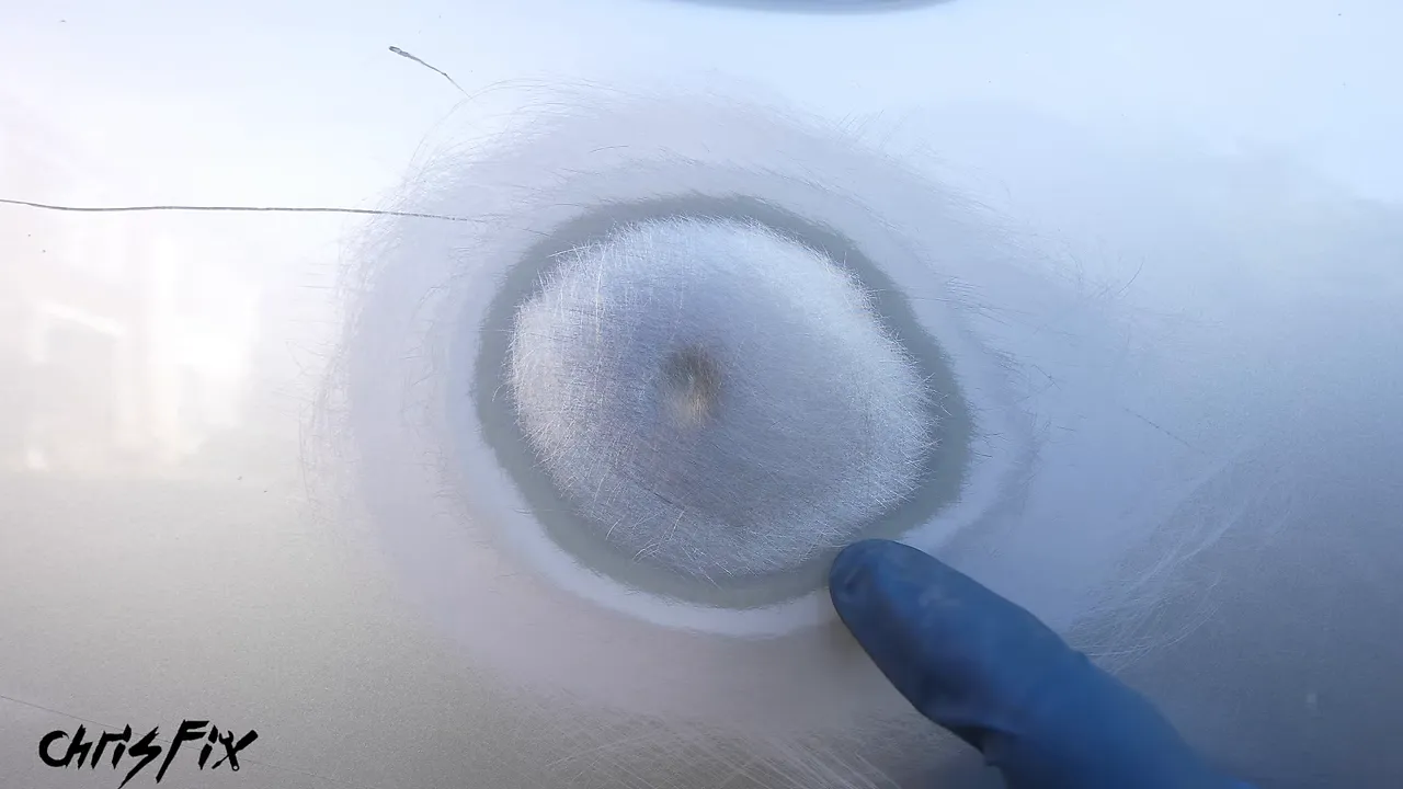 Sanded dent with exposed metal at the center and rings of surrounding paint layers