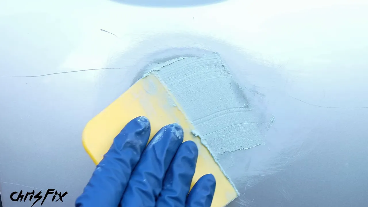 Fresh body filler covering a dent within a sanded area below the door handle
