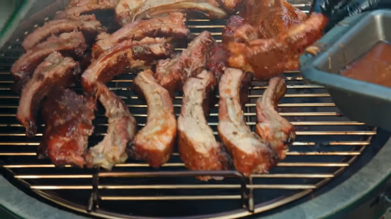 Individual ribs arranged on the grill beside a shallow pan of reddish glaze