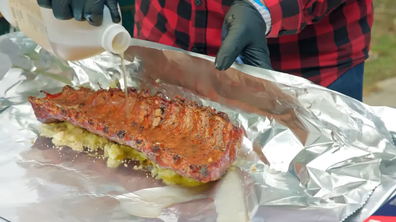 Apple cider vinegar being poured over a rack of ribs resting meat side down on butter and brown sugar
