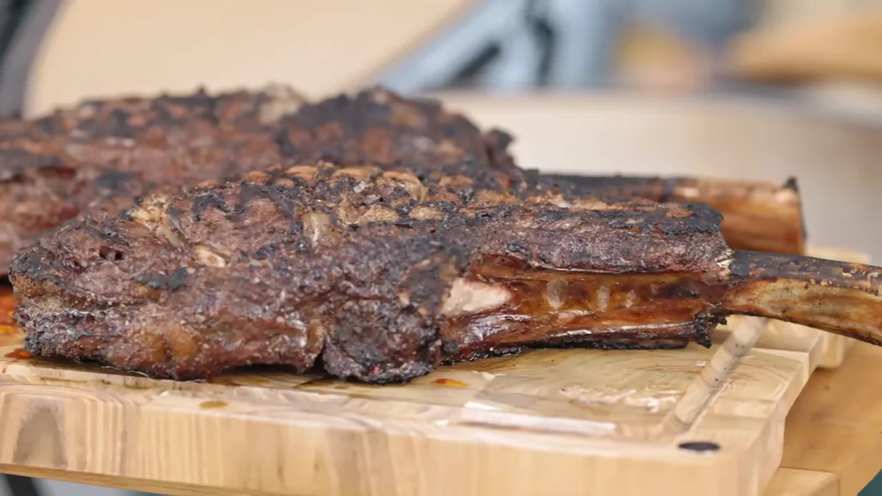 Two seared tomahawk steaks with dark browned crusts on a wooden cutting board